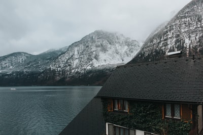 黑色和棕色油漆的2层房子附近的水体和灰色的山脉覆盖着雪在白天